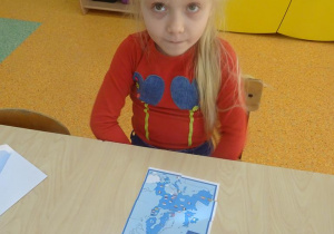 Dziewczynka układa przy stoliku obrazki z części oraz rozsypankę literową.